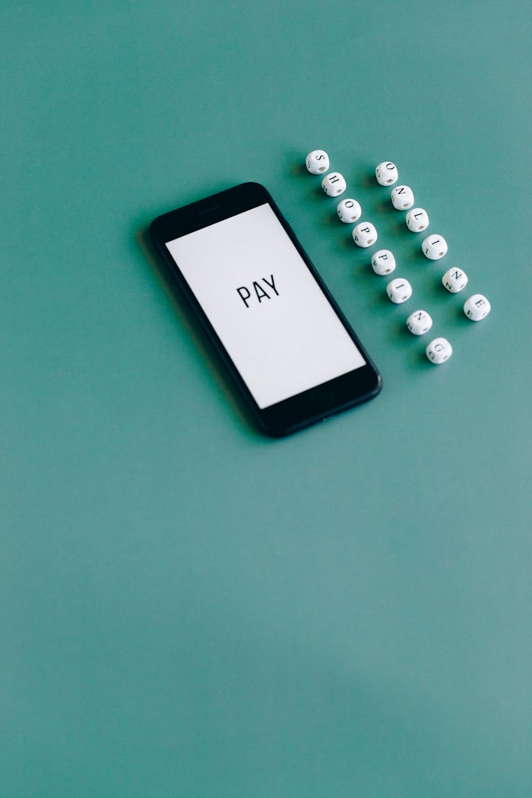 Smartphone with 'PAY' text next to beads on green background, symbolizing online payment.